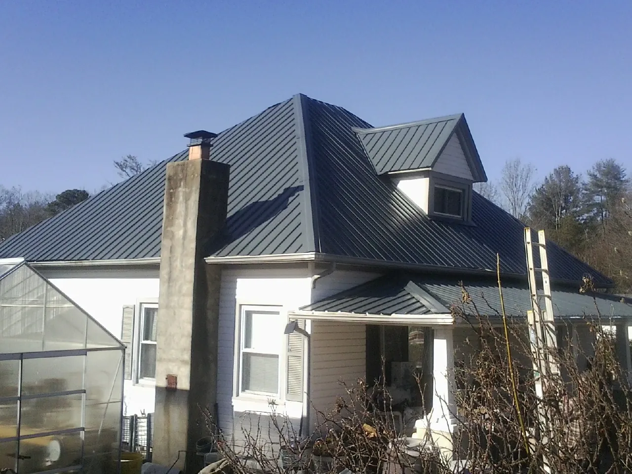 Dark blue standing seam metal roof on a white farmhouse with dormer — Slate & Tile Roof Repair by Roofing Brothers in Old Forge
