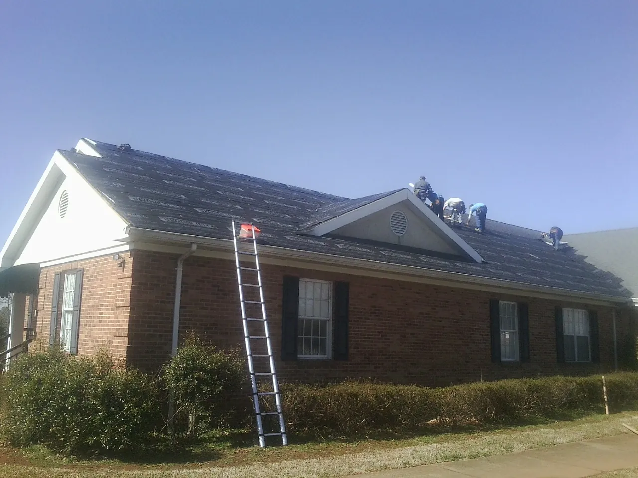 Crew tearing shingles off a brick ranch roof with a ladder set — Emergency Roof Repair work by our crew in Old Forge