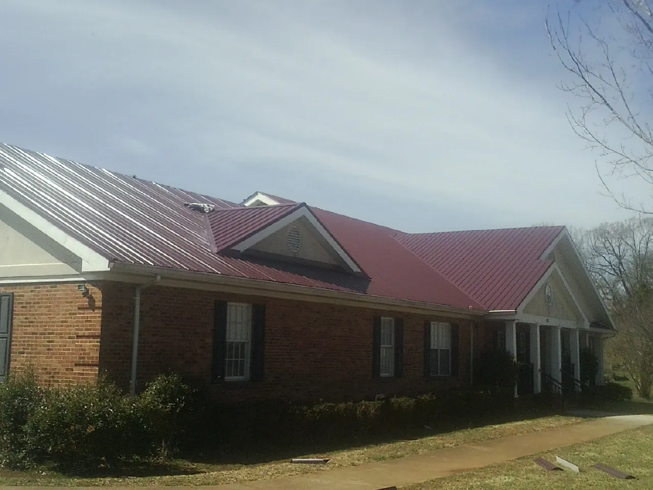Red metal roof with gabled entries on a long brick building, from a Hail Damage Roof Repair job in Old Forge