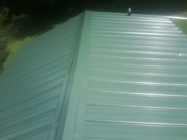New green metal panels meeting at the ridge of a roof — Flat Roof Repair work by our crew in Old Forge
