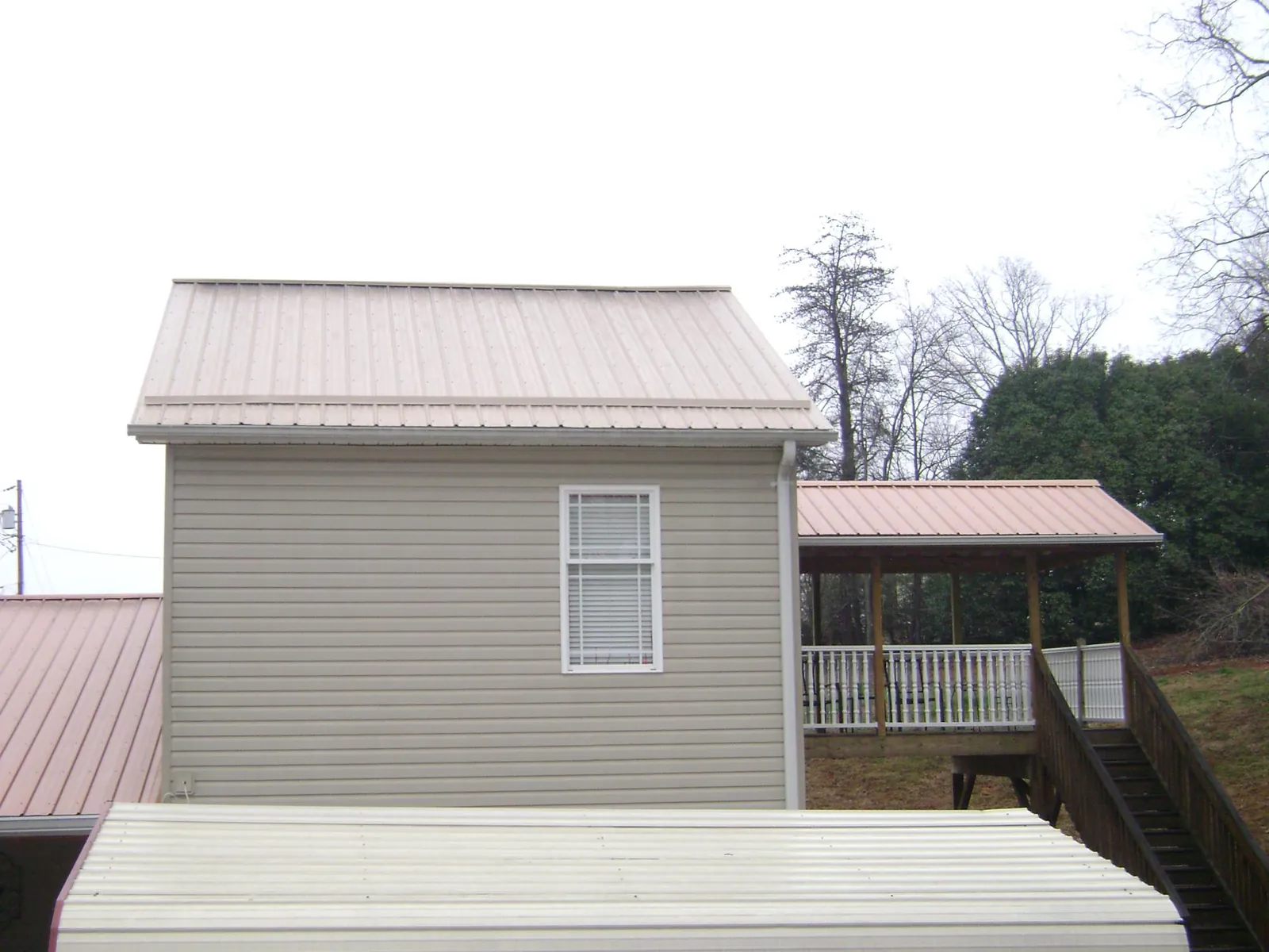 Tan metal roofs on a two story addition and attached porch, from a Roof Replacement job in Old Forge